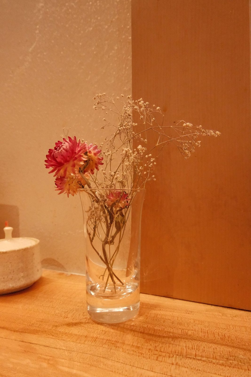 A few dried flowers in a glass on a wooden ledge