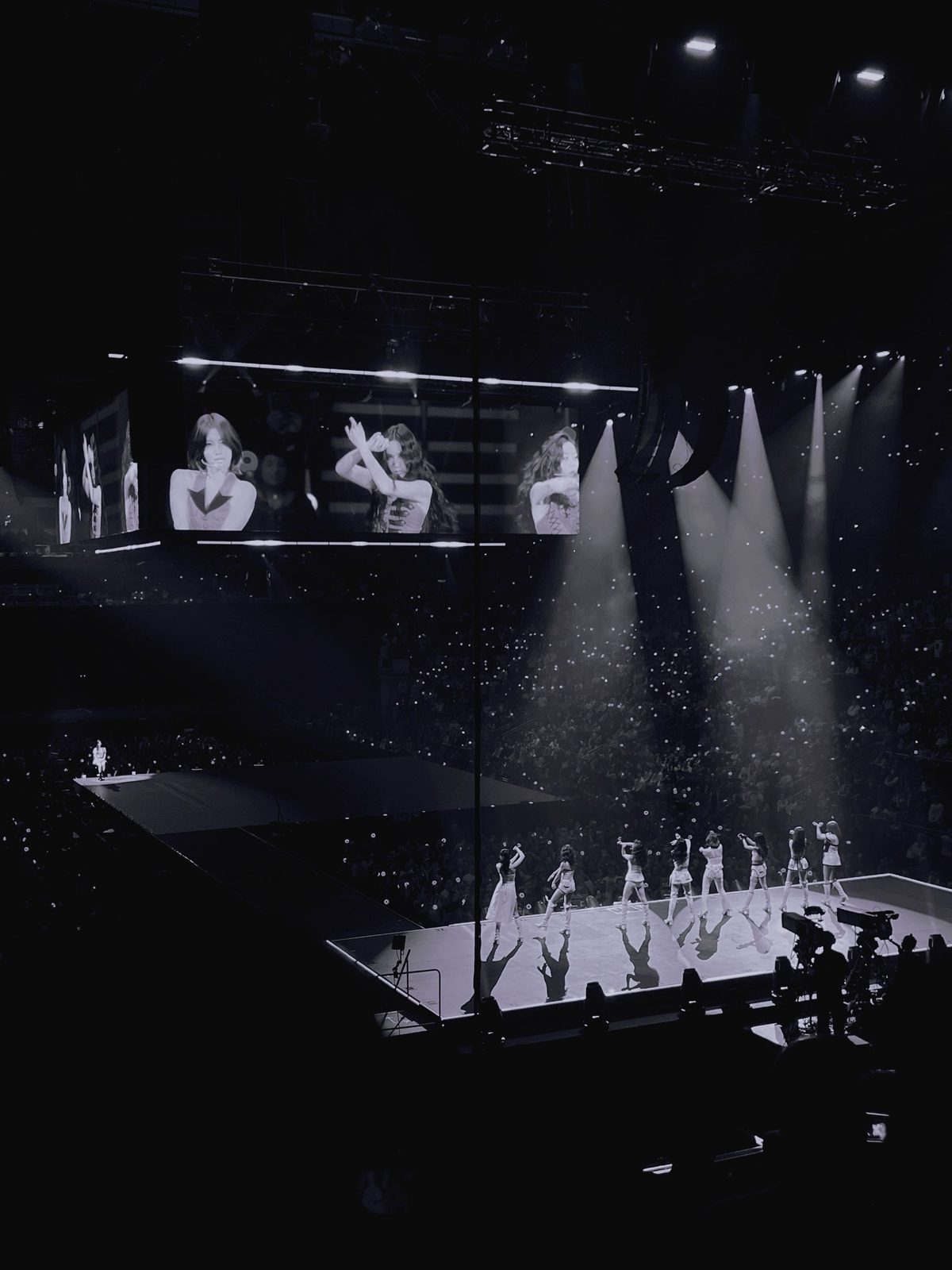 TWICE performing at the THIS IS FOR World Tour, dancers lit by spotlights in black and white