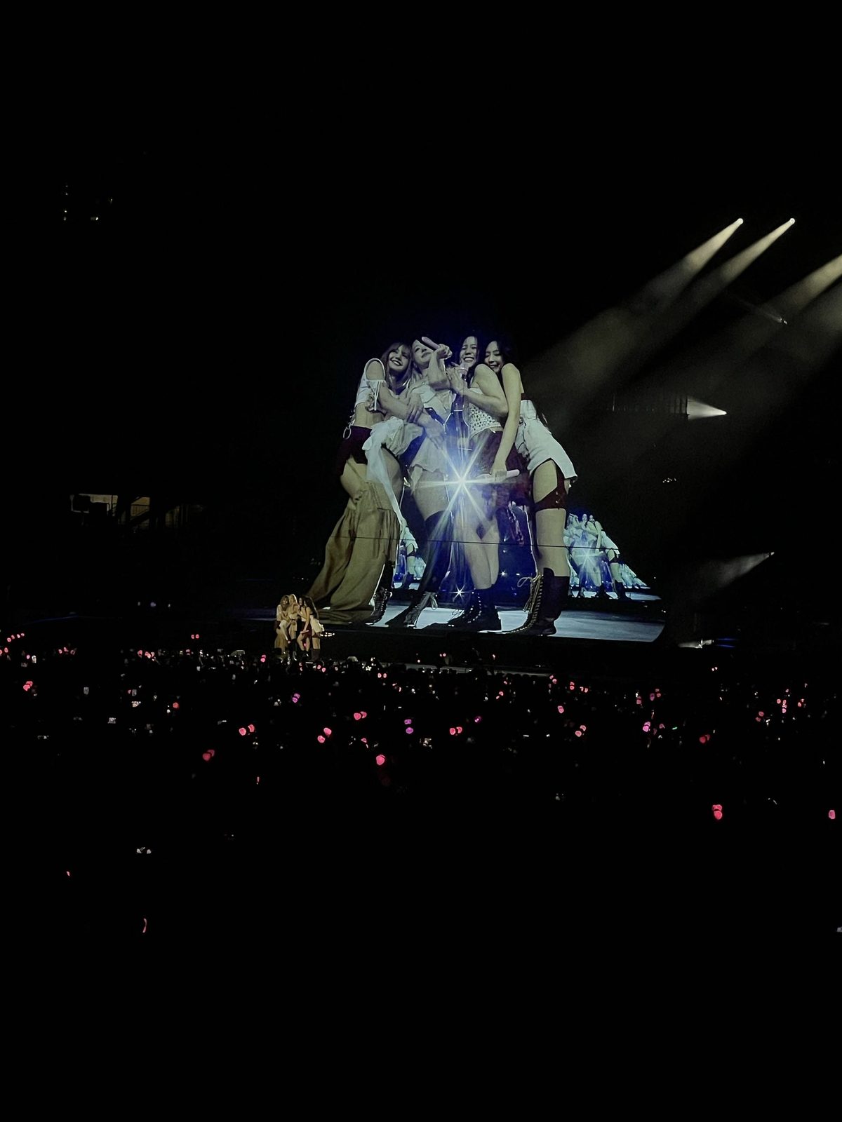 BLACKPINK huddled together on stage at the DEADLINE Tour, Jul 2025, a pink lightstick ocean in the crowd
